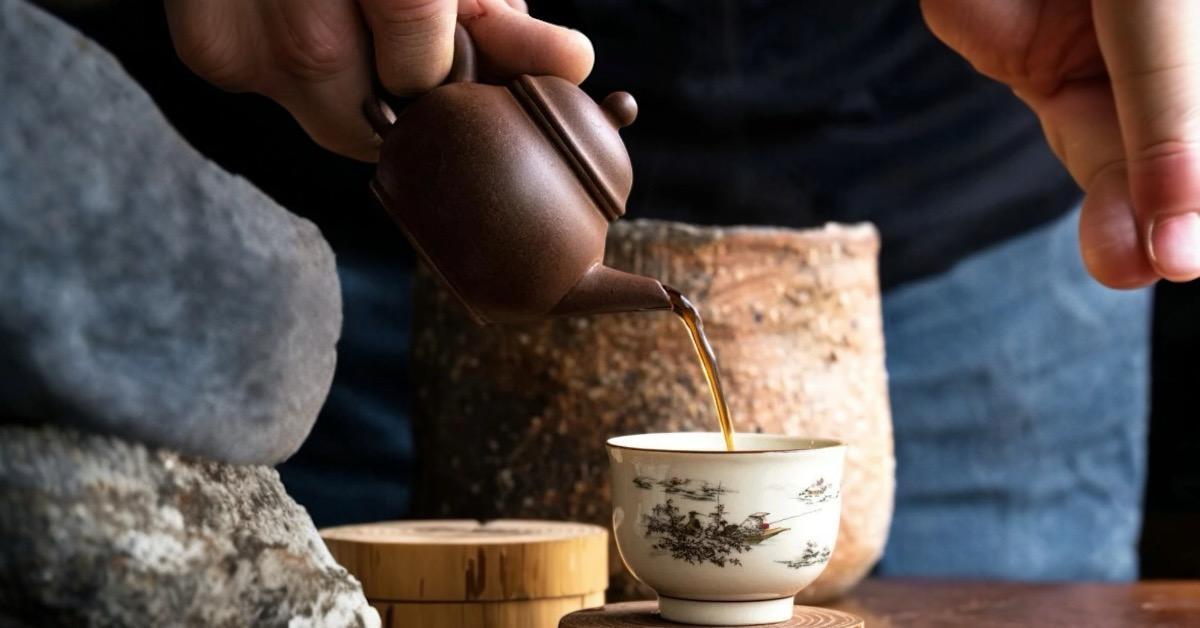 Traditional dark tea being poured from a clay teapot into a teacup, featuring fermented loose leaf tea with rich earthy tones, aged pu erh, and artisan tea craftsmanship.